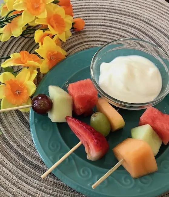 3 fruit kabobs with a small bowl of vanilla yogurt