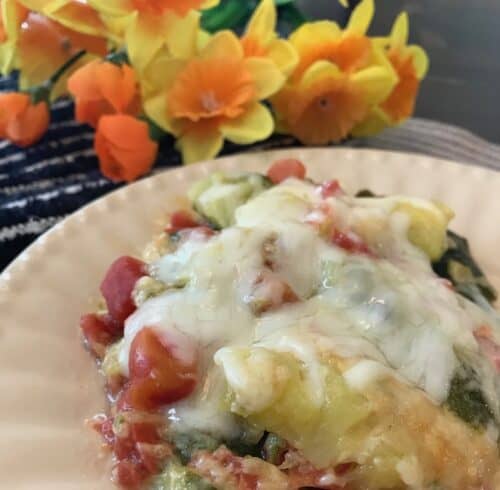Zucchini tomato casserole on a plate beside yellow flowers