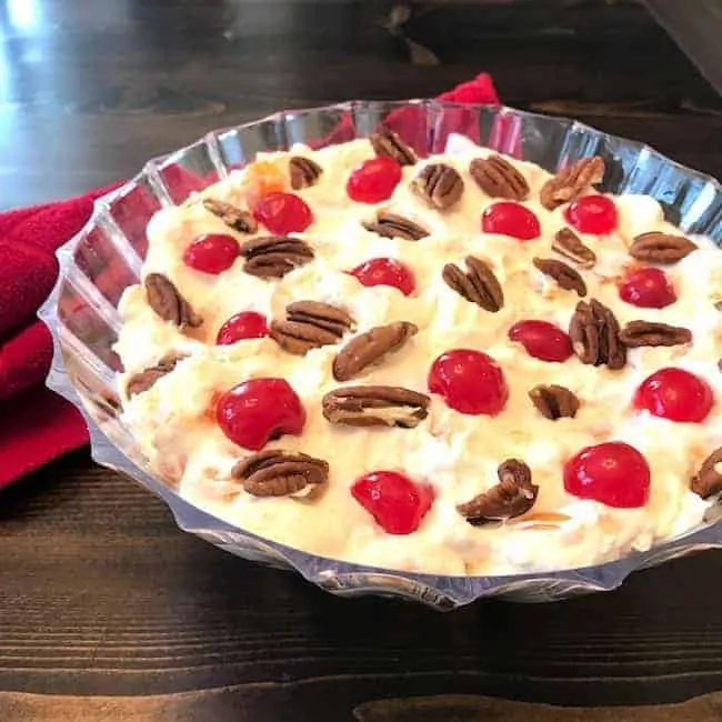 Fruit salad topped with pecans and maraschino cherries in a serving bowl