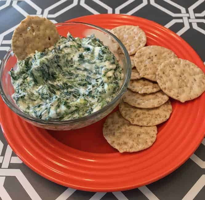 Bowl of spinach dip beside crackers on an orange plate