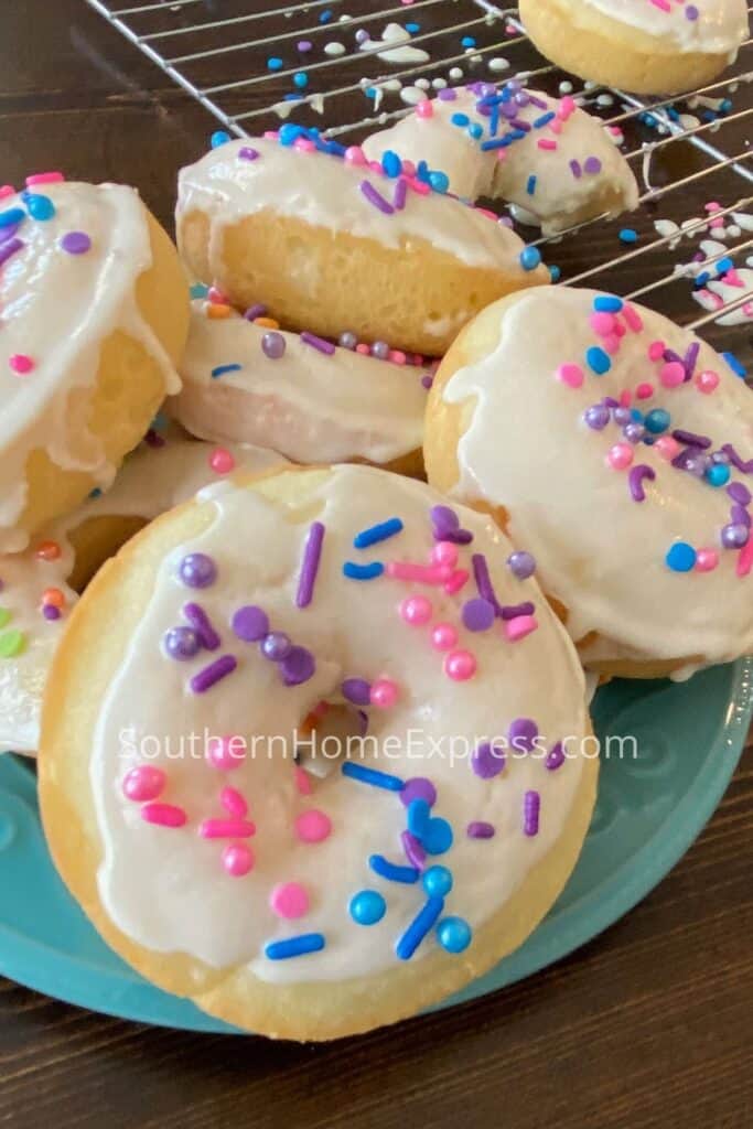 Stack of frosted donuts on a plate with sprinkles all over the tops