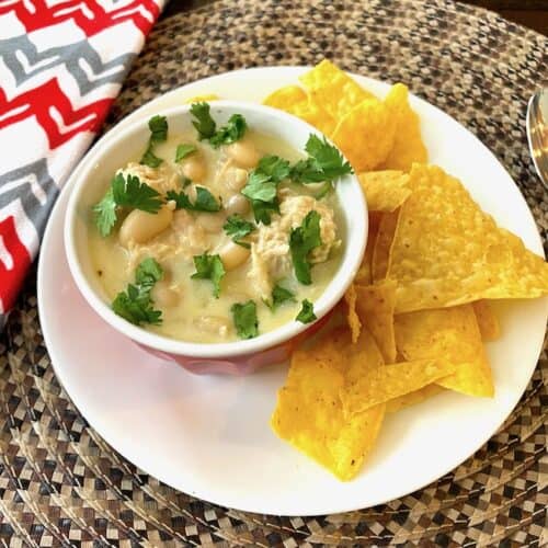 White chicken chili garnished with cilantro in a bowl on a plate with tortilla chips