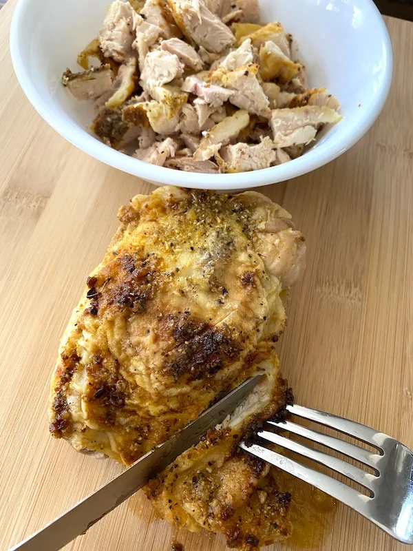 cutting a chicken thigh with a bowl of chopped chicken next to it.