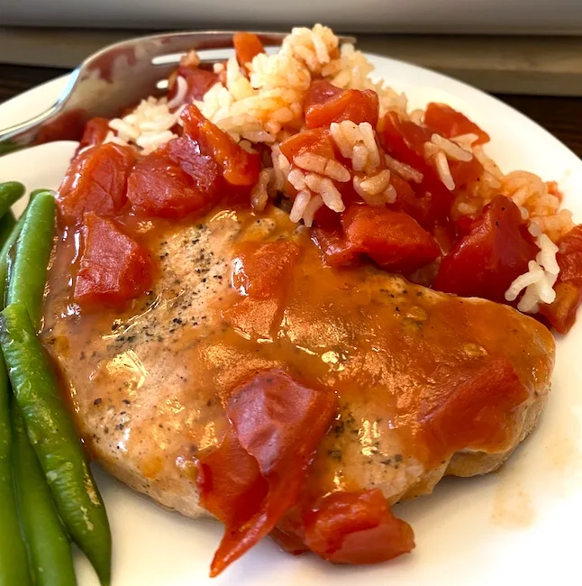 pork chop with tomato gravy on a plate with green beans