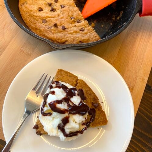 slice of skillet chocolate chip cookie on a plate next to the cookie pan