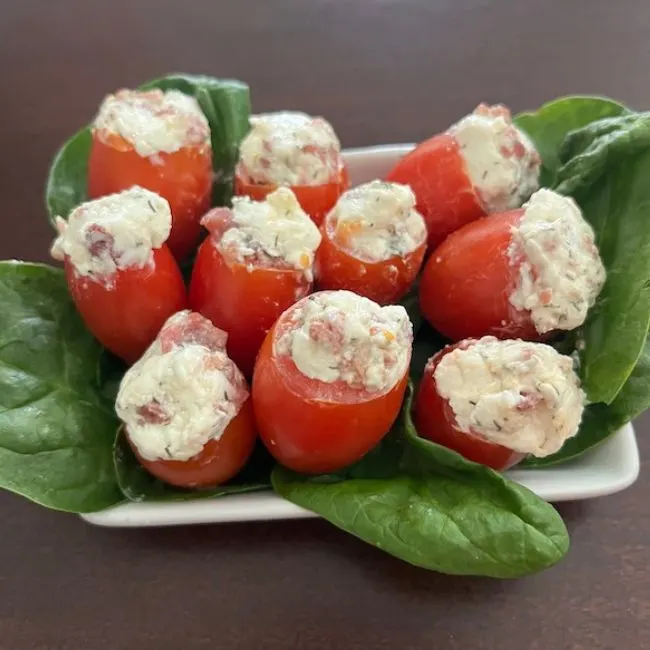 small plate of bacon and cream cheese stuffed tomatoes on a bed of spinach leaves