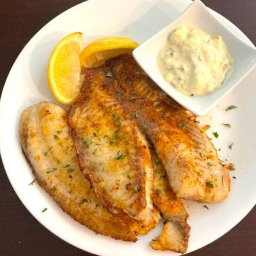 plate of seasoned tilapia with tartar sauce and lemon wedges