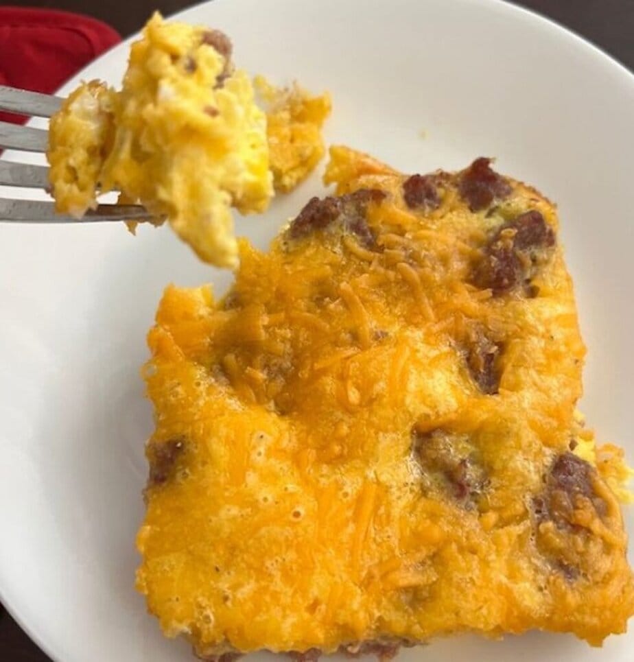 forkful of breakfast casserole beside a slice of breakfast casserole on a plate