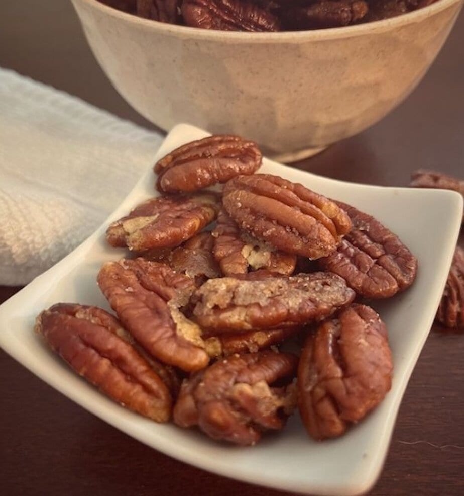 small plate of pumpkin pie spiced pecans beside a bowl
