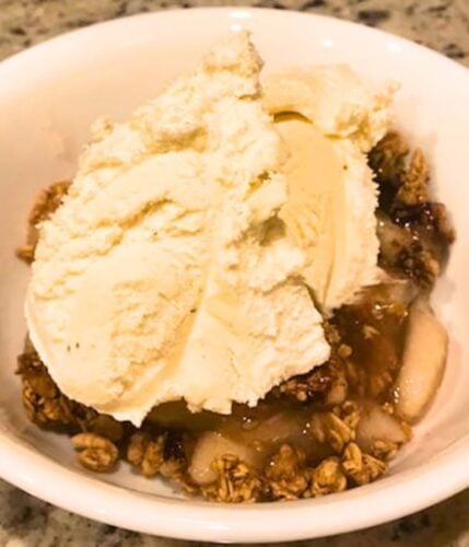 bowl of granola fruit crisp topped with vanilla ice cream