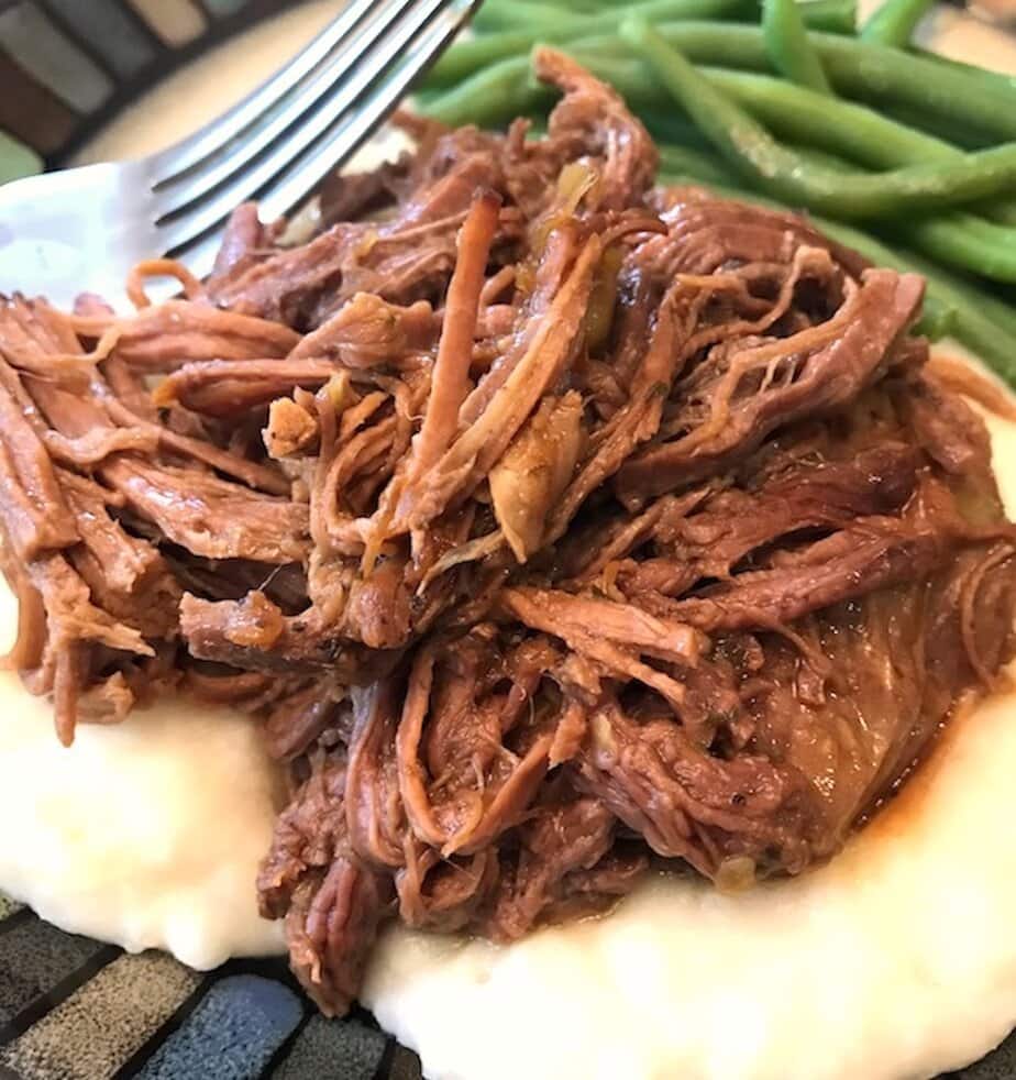 shredded Mississippi pot roast over a bed of mashed potatoes with a side of green beans