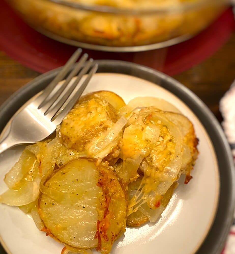 serving of cheesy parmesan potato bake on a plate beside a casserole dish