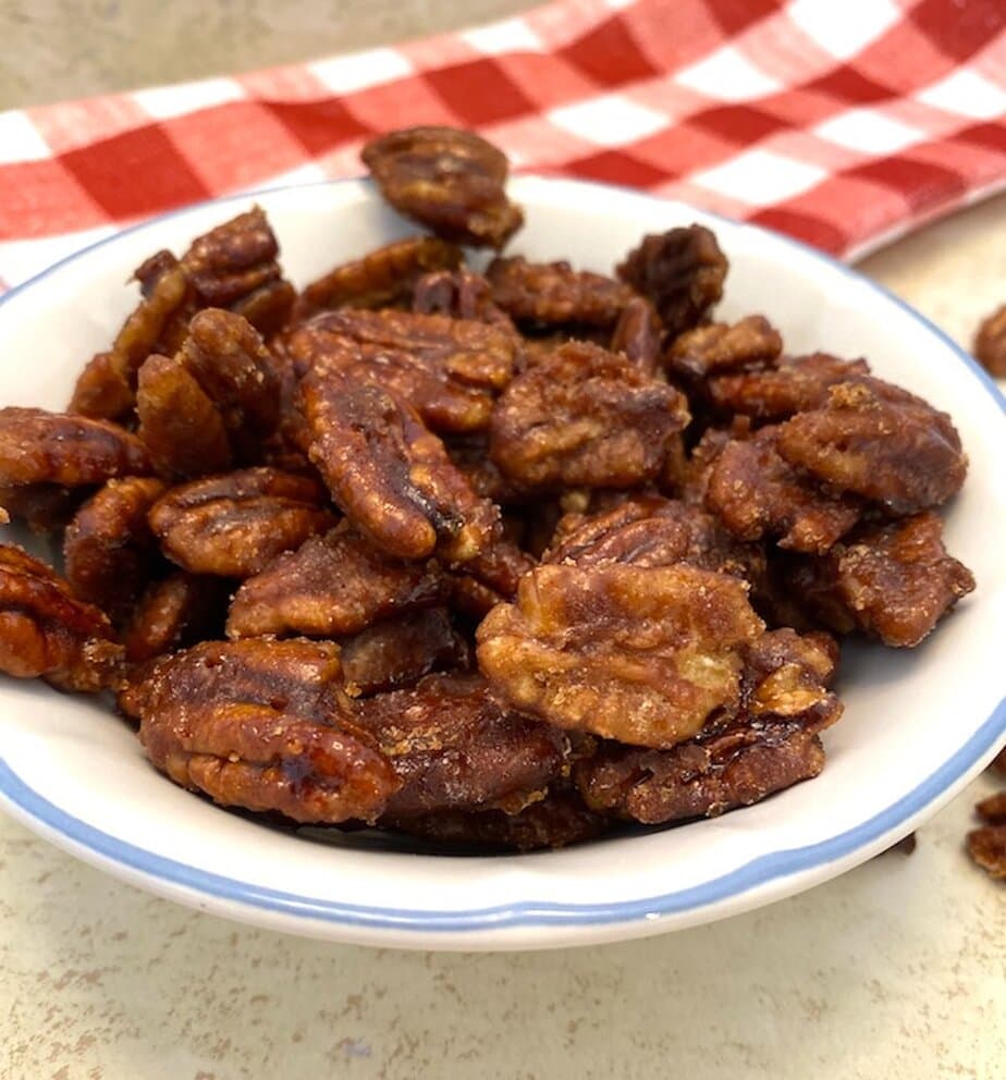 bowl of candied pecans beside a red and white checkered dishtowel