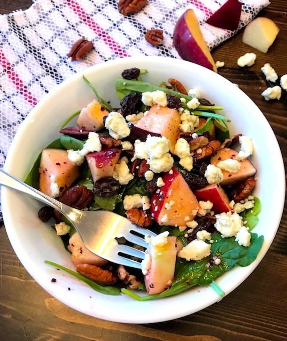 fork in bowl of apple spinach salad with blue cheese crumbles