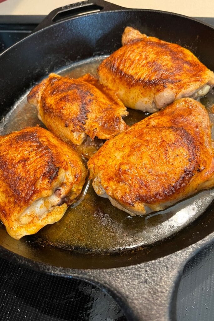 chicken thighs cooking in a cast iron skillet