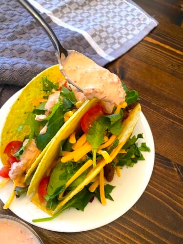spooning baja sauce over tacos on a plate