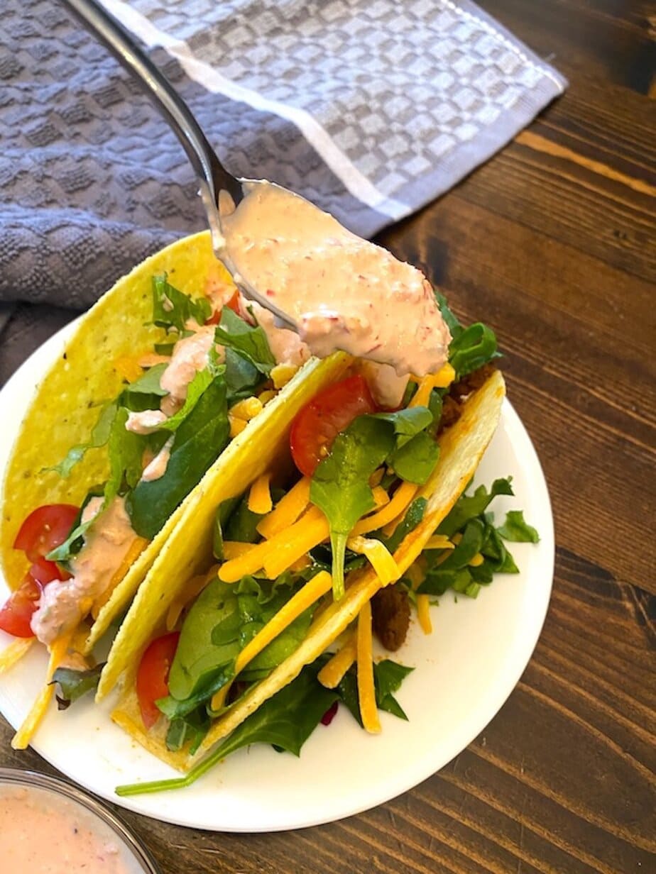 spooning baja sauce over tacos on a plate