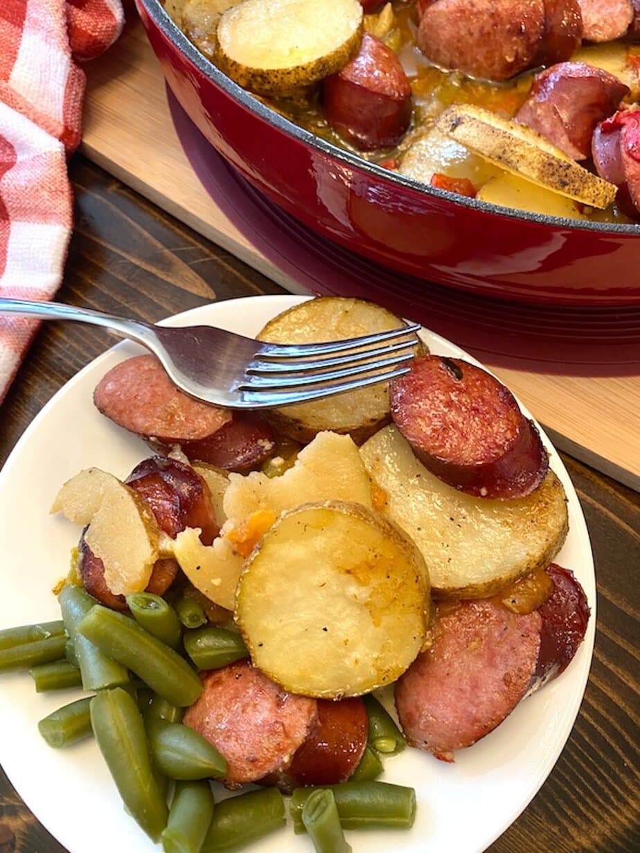 pan and plate of smothered sausage and potatoes with a side of green beans