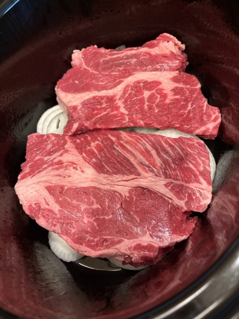 chuck steak on top of onion slices in Crock Pot