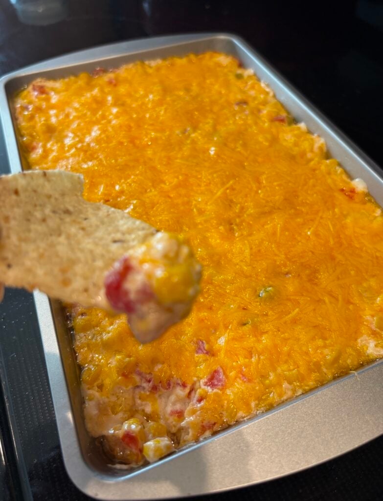 chip scooping cream cheese rotel corn dip in a pan