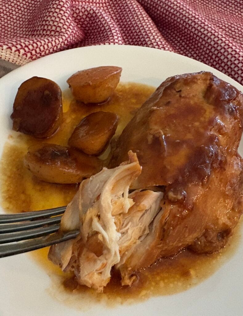 fork of barbecue chicken over a plate of chicken and potatoes