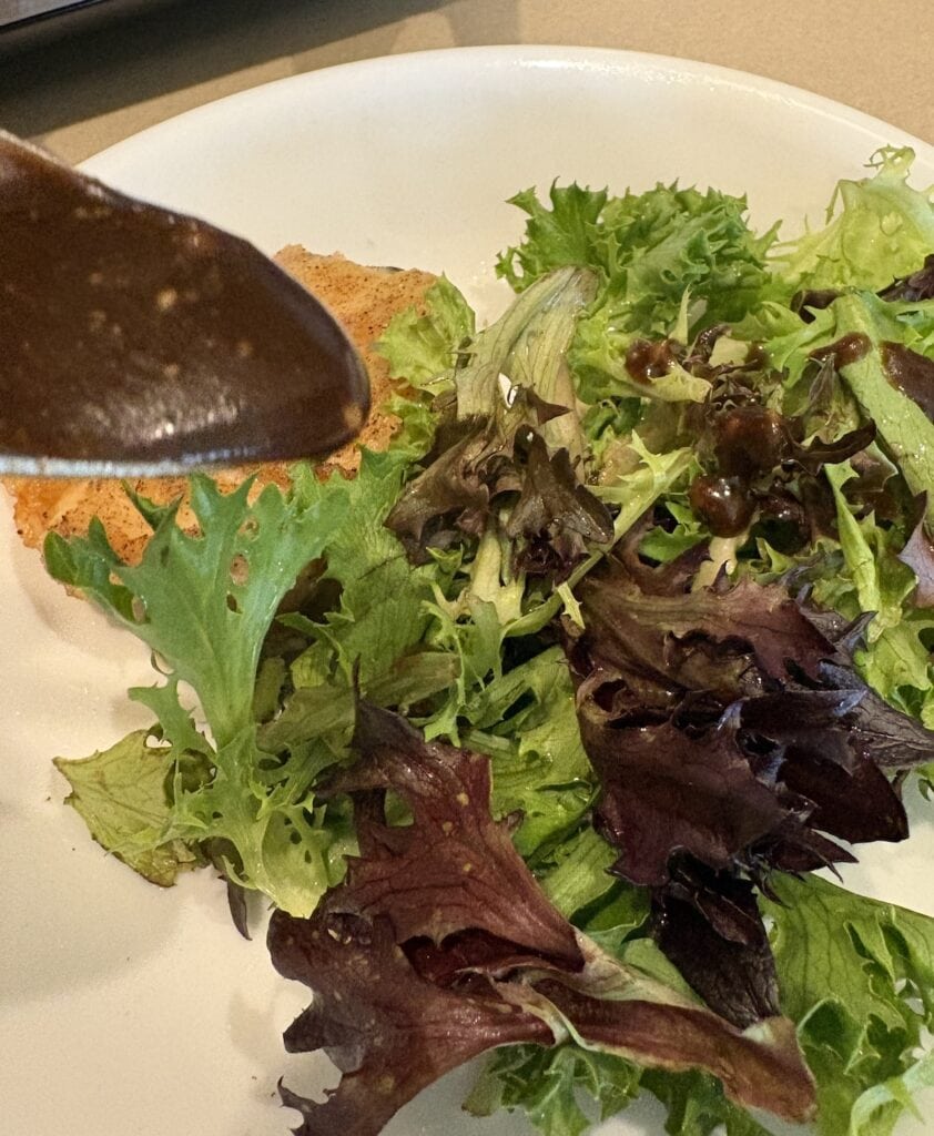 spoon of balsamic vinaigrette over spring mix salad