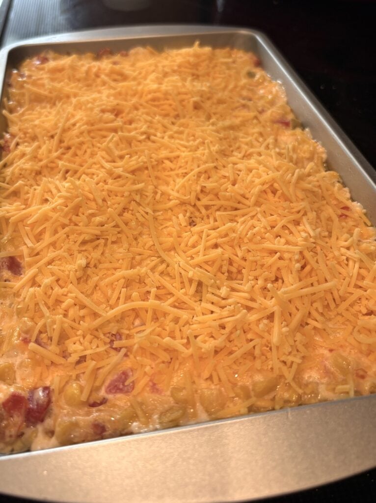 shredded cheese over cream cheese rotel corn dip in a pan